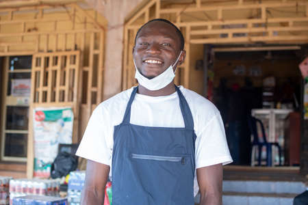 portrait of an african small business owner wearing a face mask in front of his store and smiling