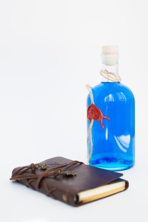 glass bottle with blue Curacao alcohol color on white background. brown leather notebook with white sheets.の写真素材