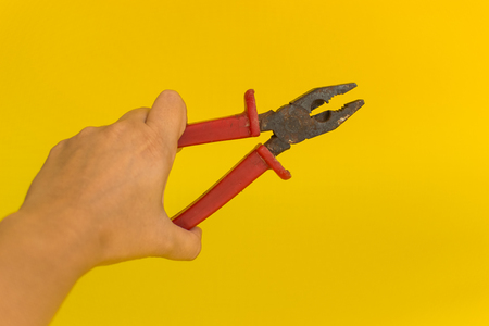 hand holding red pliers on yellow background