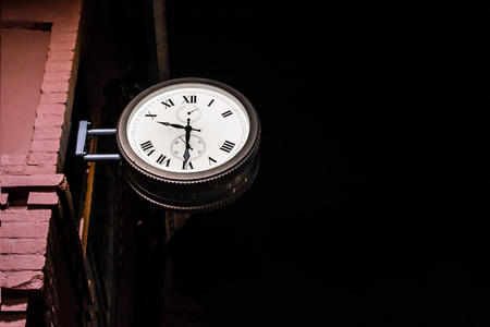 street clock attached to a brick wall night.