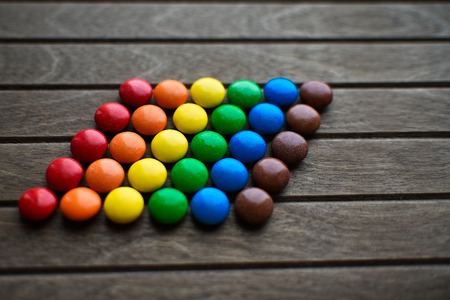 chocolates in glaze stacked in LGBT flag on wooden background.