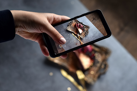 girl's hand shoots food dessert on the phone. chocolate souffle pudding cake filled with fresh berries on the Golden trayの写真素材