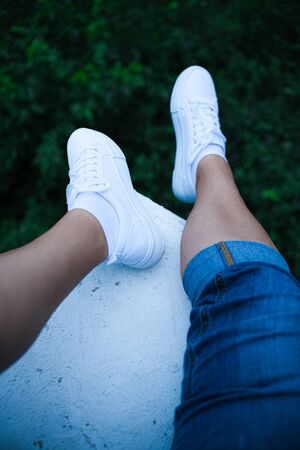 legs in jeans white sneakers over the green forest top view