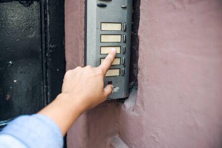 hand in a denim jacket reaches for the doorbell. finger presses the doorbell. the street door.の写真素材