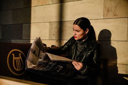 Young beautiful brunette girl posing at sunset on a wall background on a city streetの写真素材