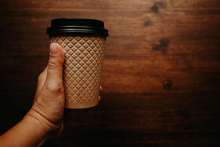 a dark-skinned mans hand holds a paper Cup against a tree backgroundの写真素材
