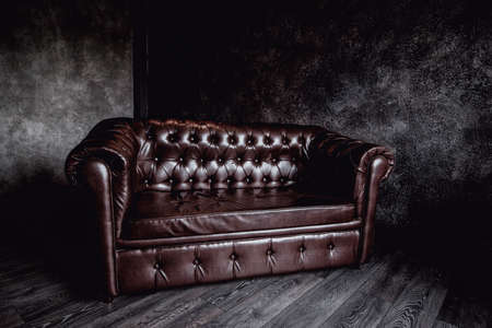 big brown leather sofa in a dark room gray walls concreteの写真素材