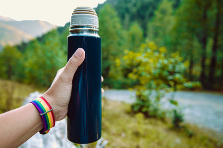 Close-up of a flask bottle with hot tea in the autumn nature in a womans hand