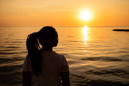 Woman Looking at the Sunset by the Sea. Silhouette of a dreamer girl looking hopeful at the horizonの写真素材
