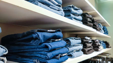 Jeans of different colors, textures and shades lie in neat piles on the window counter of the brand fashion store.の写真素材