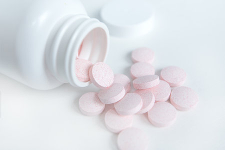 Pink pills pouring out of the white bottle. snowy white backgroundの写真素材