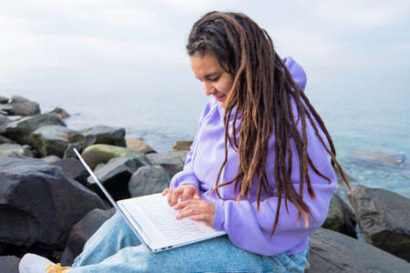 girl hair dreadlocks. sea coast winter using laptop computer on a beach. Freelance work, vacations, mindfulness, business, people, technologies, distance studying, connection, communicationの写真素材