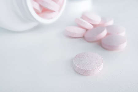 Pink pills pouring out of the white bottle. snowy white backgroundの写真素材