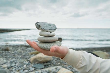 Balance of stones on the hand against the background of the sea. The concept of peace of mind, harmony, spiritualityの写真素材