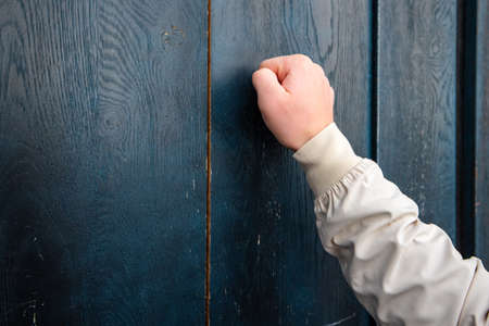 man hand in a beige jacket knocks on a blue wooden door Anybody homeの写真素材
