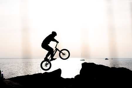 silhouette of an athlete on a bmx against the background of the sea at sunset shot from behind a fenceの写真素材