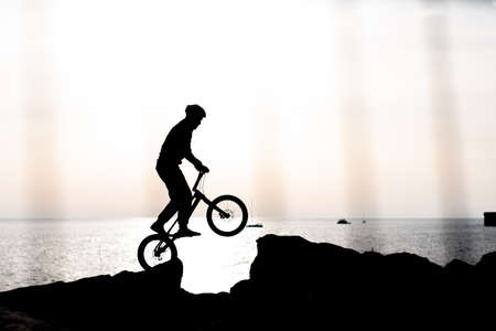 silhouette of an athlete on a bmx against the background of the sea at sunset shot from behind a fenceの写真素材