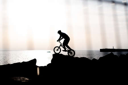 silhouette of an athlete on a bmx against the background of the sea at sunset shot from behind a fence.のeditorial素材