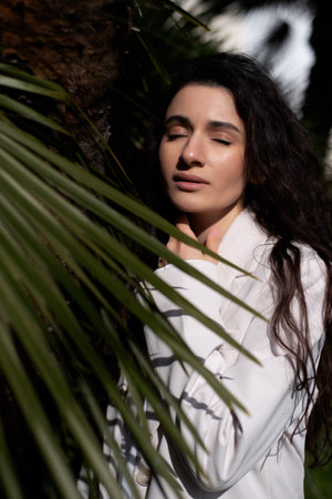 dark-haired brunette in a white business-style suit poses in palm trees. vertical photo.の写真素材