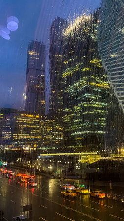 Silhouettes of big towers of the business center behind the wet glass, where on the street cloudy and rainの写真素材