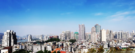 A panoramic view of Macau, China, featuring a mix of modern skyscrapers and older buildings under a clear blue sky, with a river cutting through the urban landscape.の写真素材