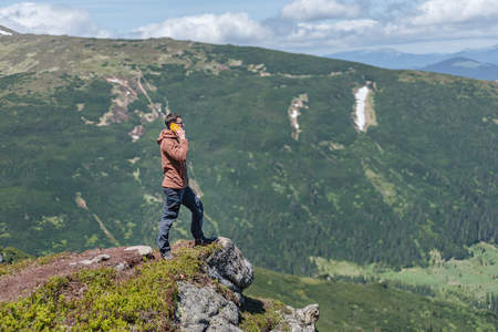 DZEMBRONYA, UKRAINE â JUNE 16, 2016: A young stands on the cliff of a mountains and speaks via smartphone.のeditorial素材