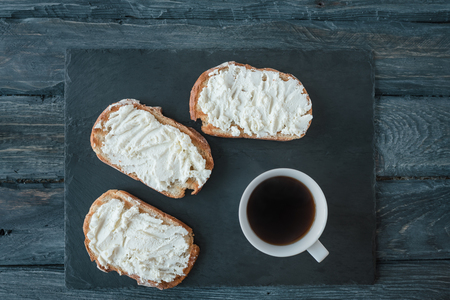 Homemade sandwiches with cream-cheese on a black slate board that lies on a black wooden table. Breakfast with black coffee.の写真素材