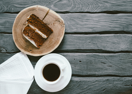 Piece of homemade cake and coffee on a black wooden table. Biscuit cake, black coffee and napkin on a wooden table. Place for textの写真素材