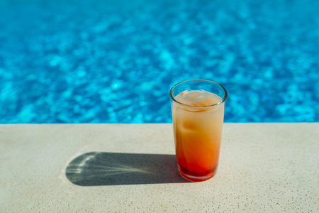 Glass with orange cocktail in front of a swimming pool with clear water. Close-up photo. Place for textの写真素材