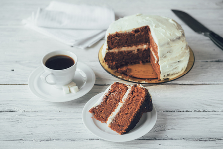 Piece of homemade cake and coffee on a white wooden table. Biscuit cake and knife at the backgroundの写真素材