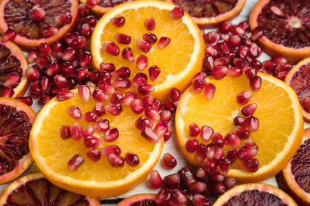 Slices of sicilian orange and common orange with scattered pomegranate seeds. Super macro photo of fruits. Top view at slices of fruits.の写真素材