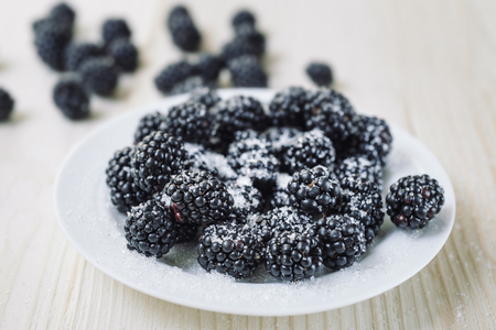 Ripe berries of dewberry on a white table on a wooden table. Healthy breakfast with vital vitamins. Ripe blackberry powdered with sugar.の写真素材