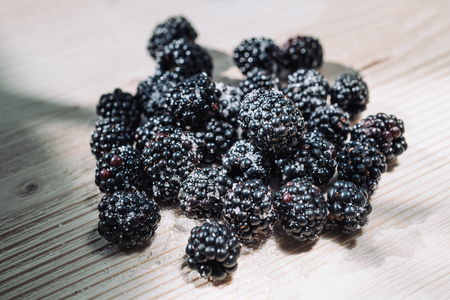 Ripe berries of dewberry on a wooden table. Healthy breakfast with vital vitamins. Ripe blackberry...