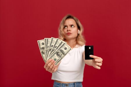 Portrait of a girl with curly blond hair in a white t-shirt standing on a red background. Model with...