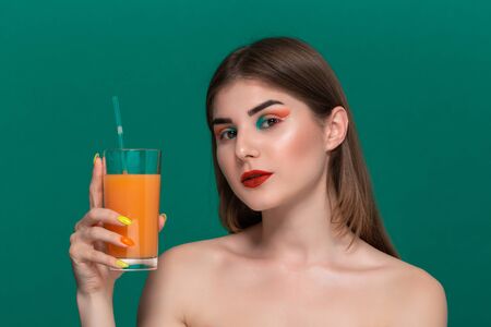 Closeup portrait of beautiful young woman with bright color make-up holding orange juice near the...