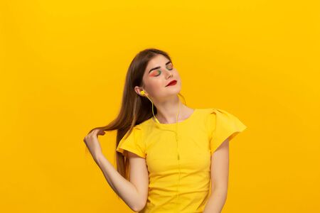 Happy young model in a yellow tee listens to music with wired headphones standing over yellow background. Place for advertisementの写真素材