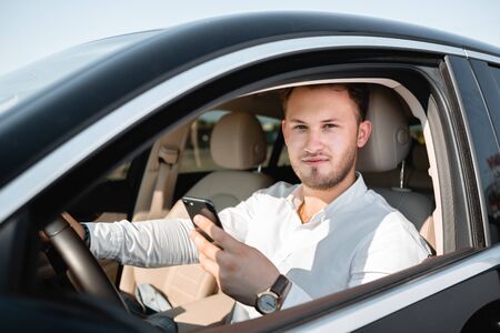 Young businessman smiling looking at mobile phone while driving a car.の写真素材