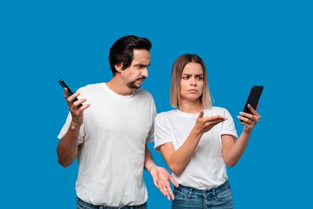 Brunet man in white tees and blue jeans is shocked looking at the smartphone screen of a blond woman.の写真素材
