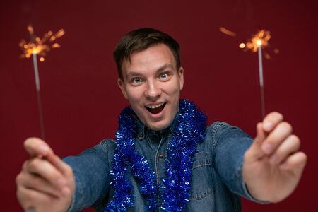 Excited man in a blue jeans shirt holding Bengal lights celebrating Christmas and New Year. Having a good time at Christmas party.の写真素材