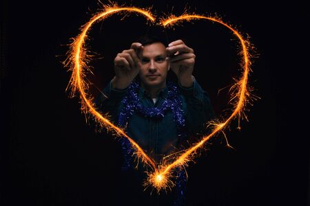 Man in a blue jeans shirt drawing heart shape from Bengal lights. Having a good time at Christmas party.の写真素材