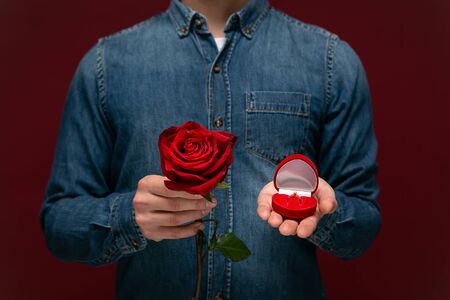 Young man making wedding proposal holding one red rose and box with engagement ring. Concept of loveの写真素材