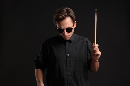 Stylish man drummer in a black shirt and sun glasses playing drums with sticks over dark background....