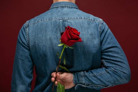 Young pretty man making surprise to his beloved hiding one red rose. Making present to girlfriend in...