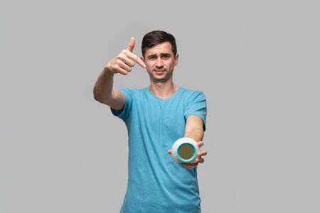 Young brunet man pointing with finger at the alarm isolated over grey background. Being late. Hurry...