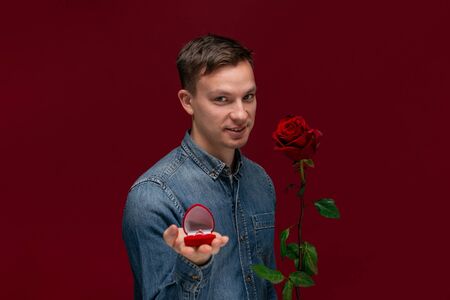 Young man making wedding proposal holding one red rose and box with engagement ring. Concept of loveの写真素材