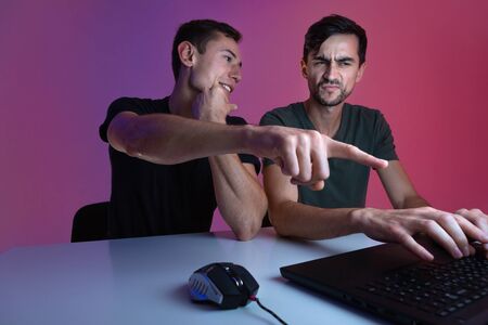 Two friends playing video game sitting in a dark room lit with neon lights. Video games championship. E-sportの写真素材