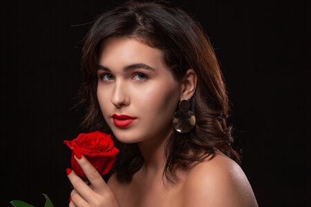 Beautiful woman with bright makeup posing isolated over black background with red rose. Image of young beautiful woman with red lipsの写真素材