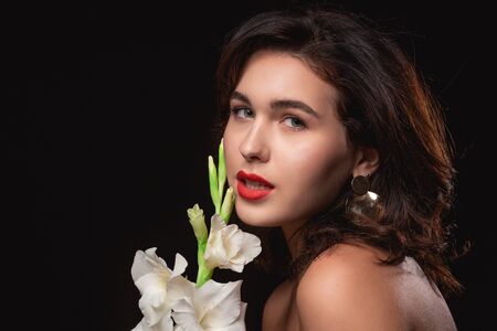Beautiful woman with bright makeup posing isolated over black background with white flower. Image of young beautiful woman with red lipsの写真素材