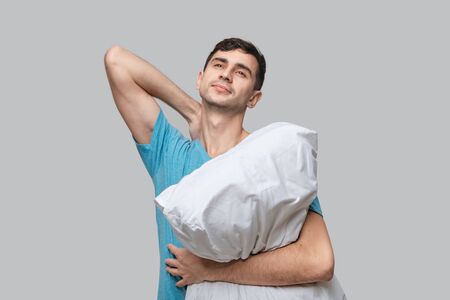 Young brunet man dreaming holding white pillow isolated over grey background. Being tired after long working day. Concept of sleeping.の写真素材