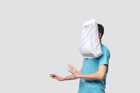 Flying white pillow hitting pretty brunet man in a blue tee. Time to go to sleep and take a rest.の写真素材